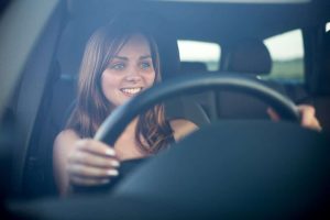 Car Insurance Banner - Young woman smiling while driving a car.