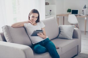Car Insurance Banner - Young woman sitting on the couch finding out about car insurance on her tablet