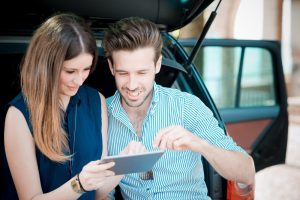 Car Insurance Banner - Young couple working out the market value of their car on a tablet while sitting in the boot