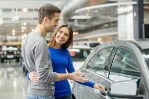 Car Insurance Banner - Young couple picking out a car to lease at a dealership